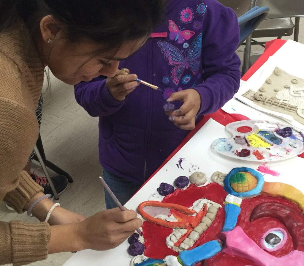 A CCATE mother and child painting the clay details of the Piedra de sol piñata