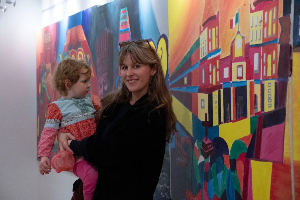 A woman holding a toddler in front of a colorful mural