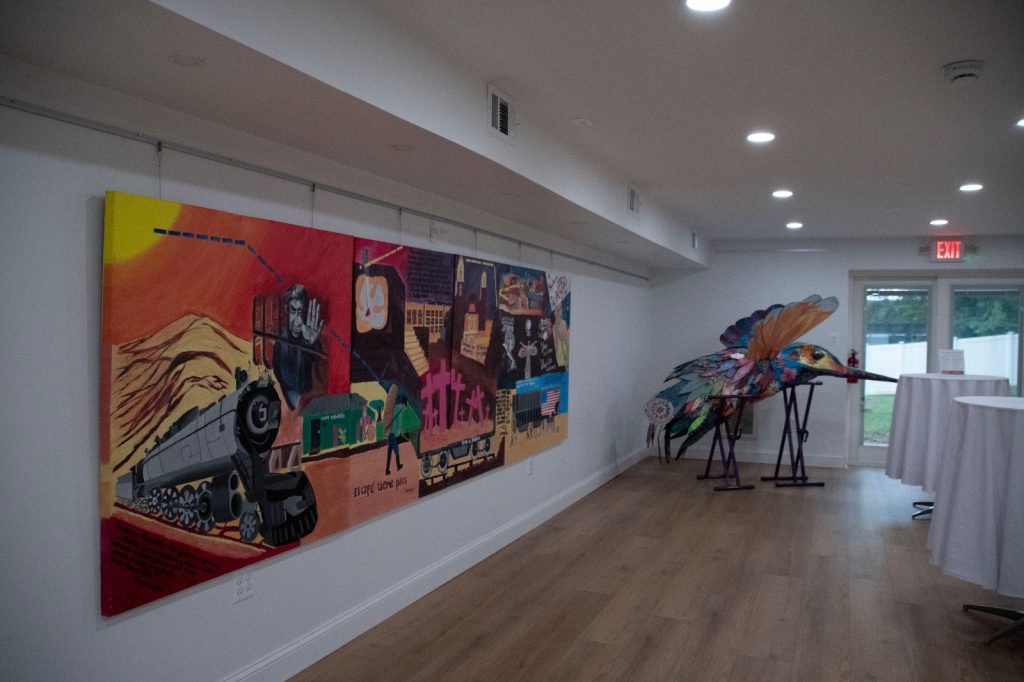 A long painted mural with a steam train beside a large colorful hummingbird sculpture