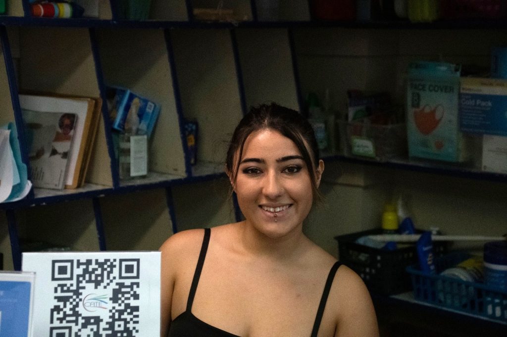 A smiling young woman at the welcome desk beside a CCATE QR code
