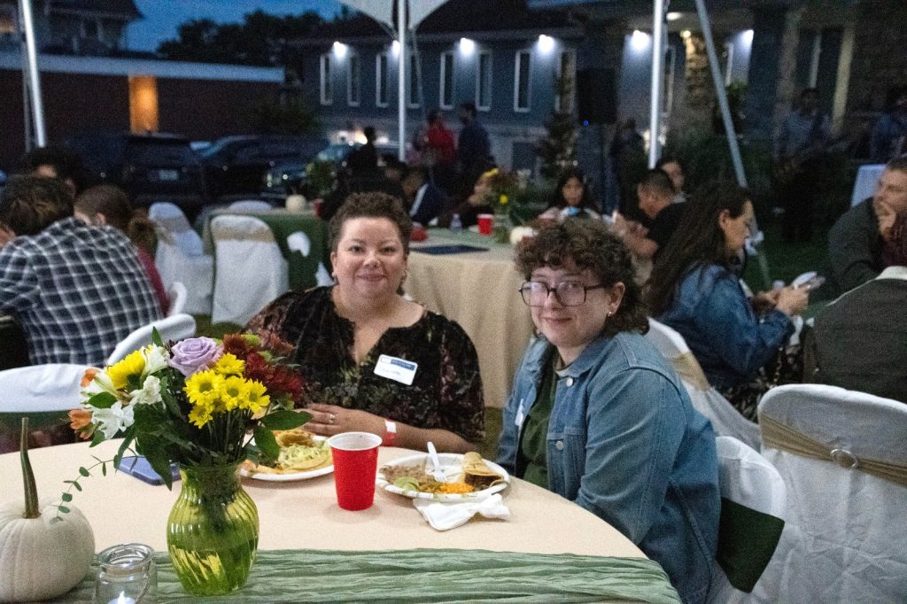 Two guests smiling at a dinner table with flowers and plates of food