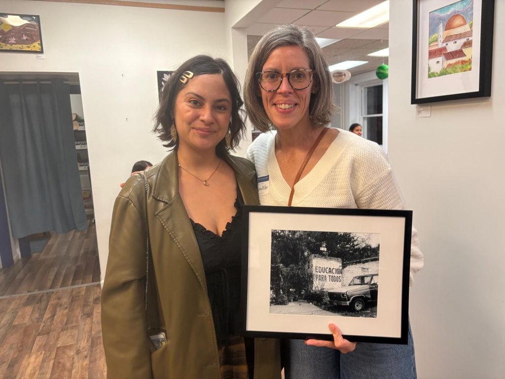 Two women holding a framed black-and-white photograph of a wall painted with the words Educación para todos