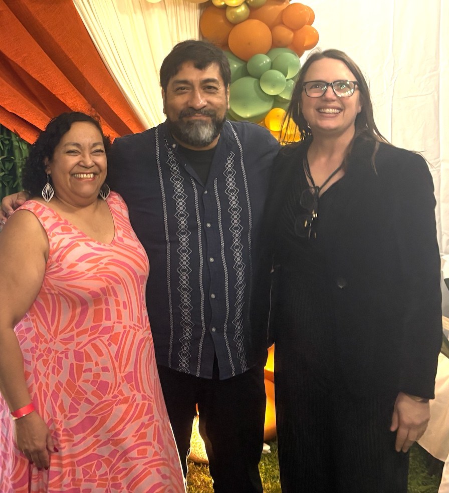 Three people smiling in front of orange and green balloons